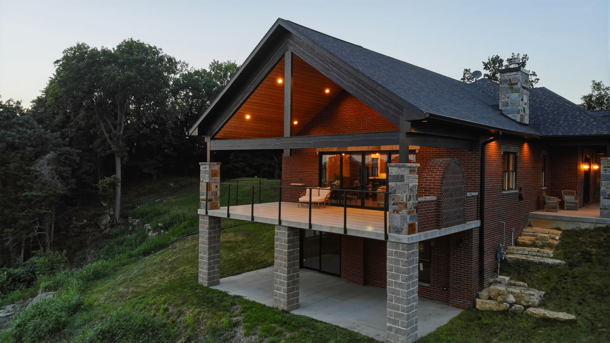 Drone view of the back of the home at dusk with the deck lit up