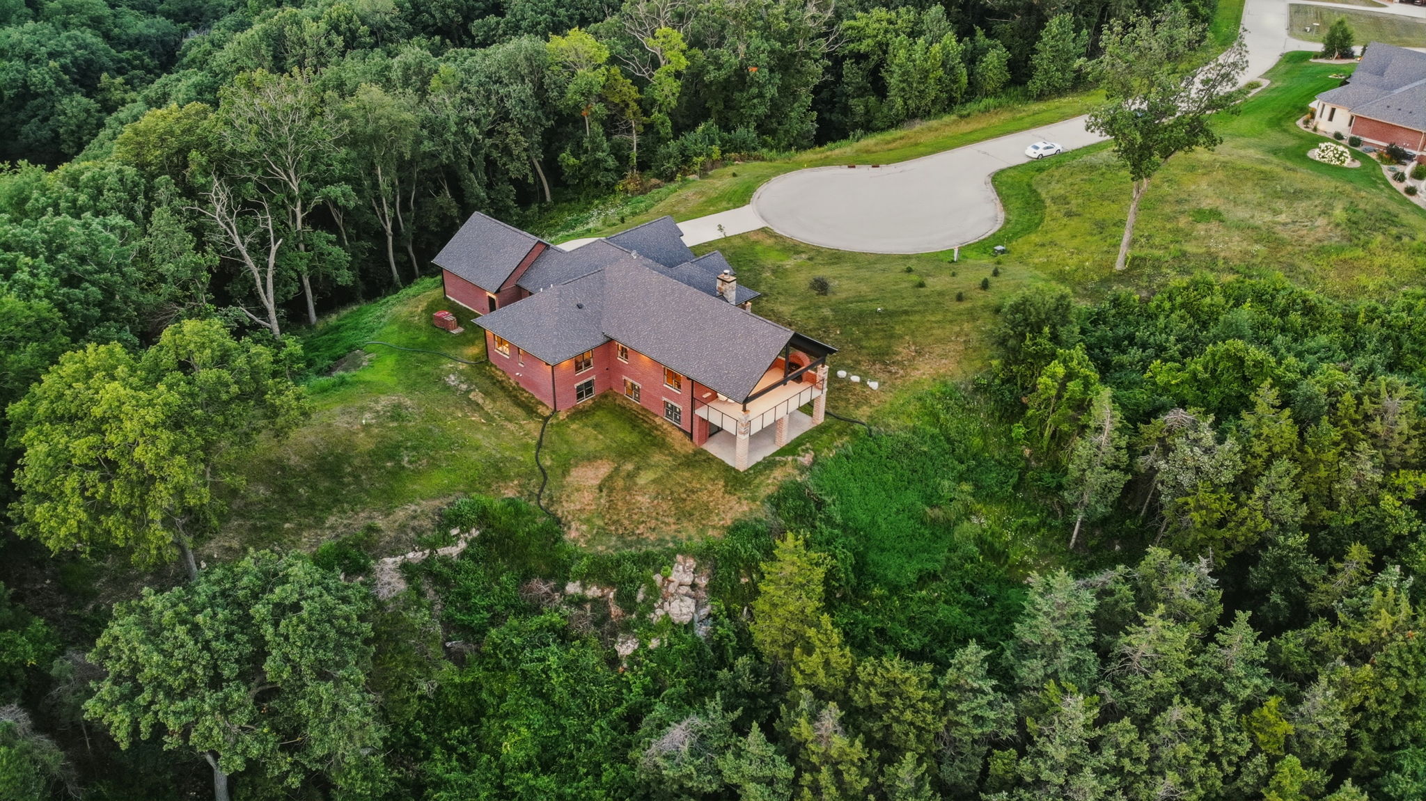 Aerial looking down on the roofline, yard and wooded bluff behind the home